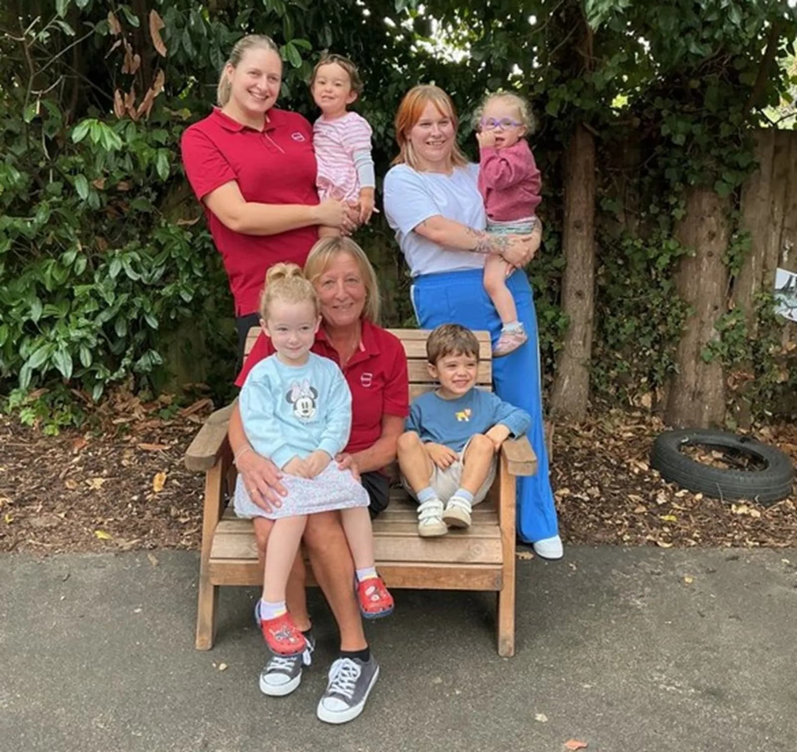 Two women holding babies, and a woman sitting on a bench with two young children on and next to her, all smiling.